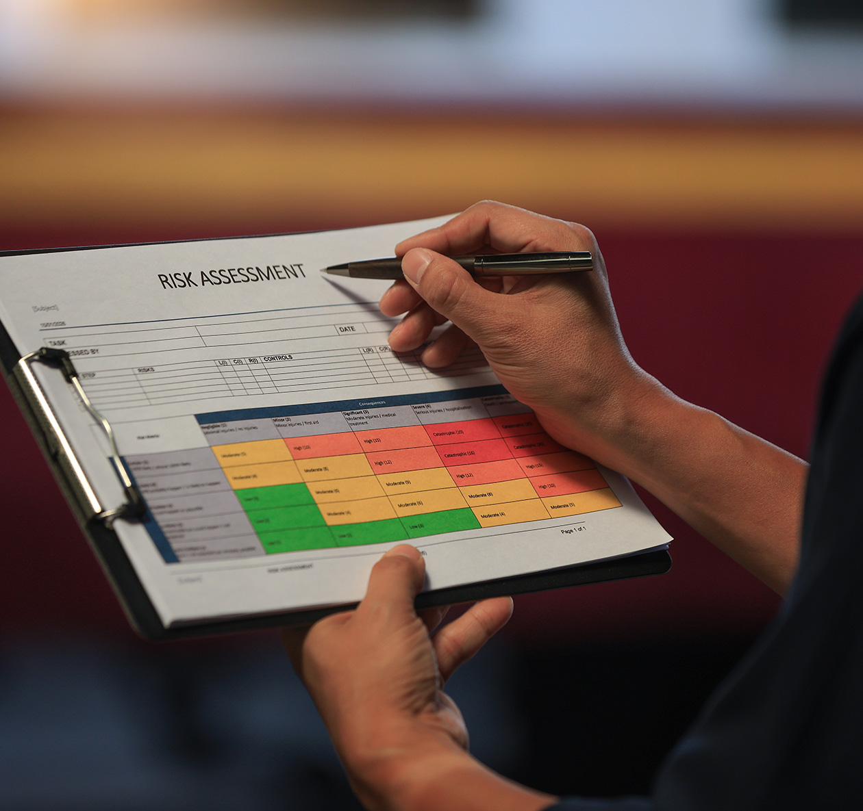 Hand holding a clipboard with a risk assessment document, featuring a color-coded table for safety evaluation, relevant to contractor compliance and documentation in construction.