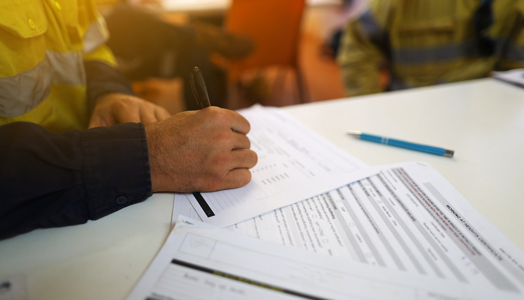 Person filling out safety documentation forms on a table, emphasizing contractor compliance and vetting processes for construction safety standards.