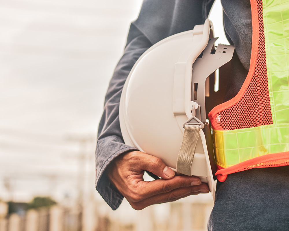 Person holding a white hard hat while wearing a safety vest, symbolizing workplace safety and OSHA compliance in a construction environment.