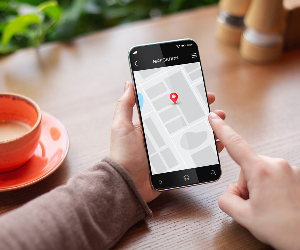 Hand holding a smartphone displaying a navigation map with a location pin, coffee cup on a wooden table, symbolizing workplace safety consulting and training accessibility.