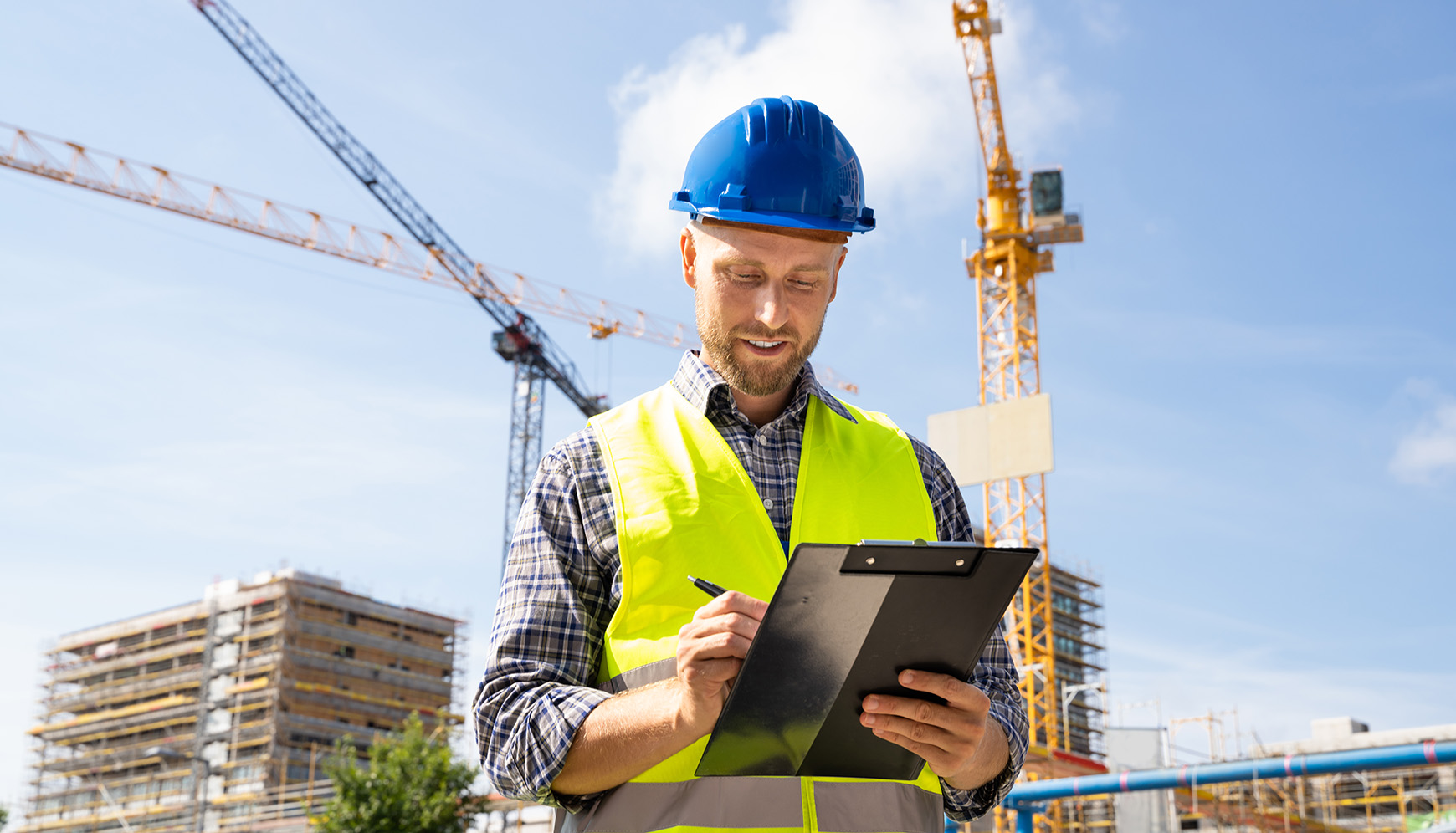 Construction safety inspector reviewing compliance checklist on job site with cranes and scaffolding in background.