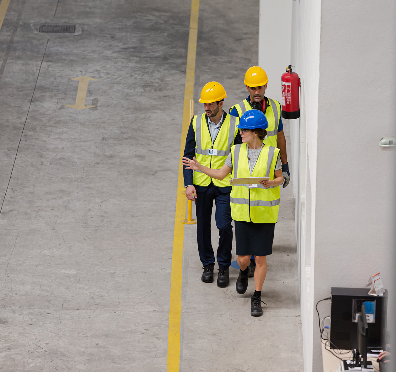 Three professionals in safety vests and hard hats conducting an OSHA compliance inspection in a workplace setting, discussing safety measures and regulations.