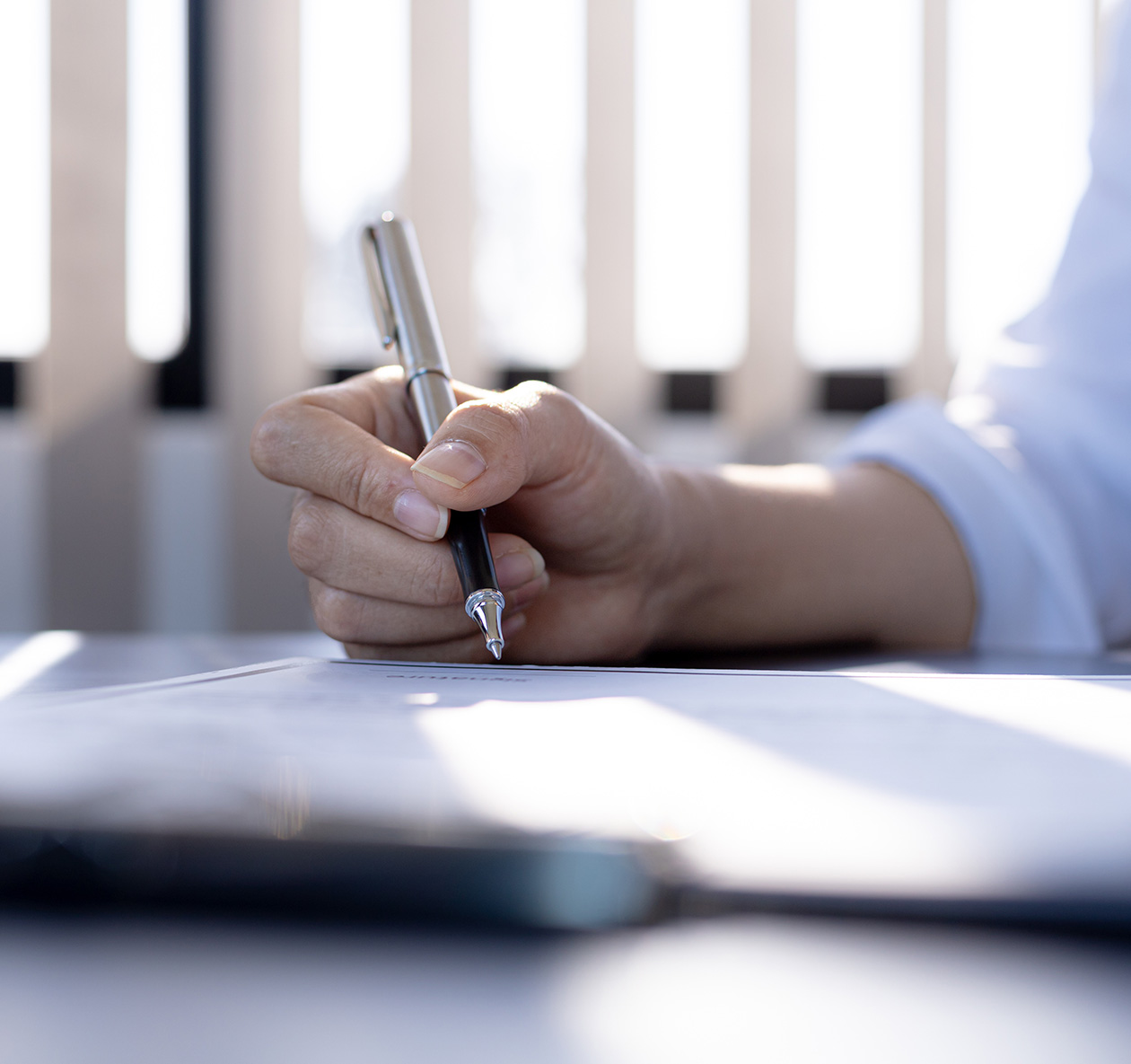 Hand holding a pen writing on a document, symbolizing contractor compliance and safety documentation for Weinstein Safety Consulting services.