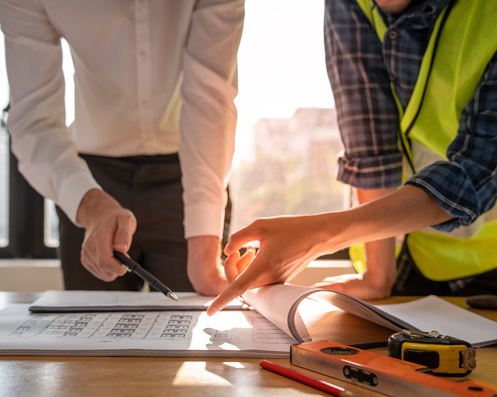 Two professionals discussing safety plans over documents on a table, with one pointing to a checklist, highlighting workplace safety and OSHA compliance.