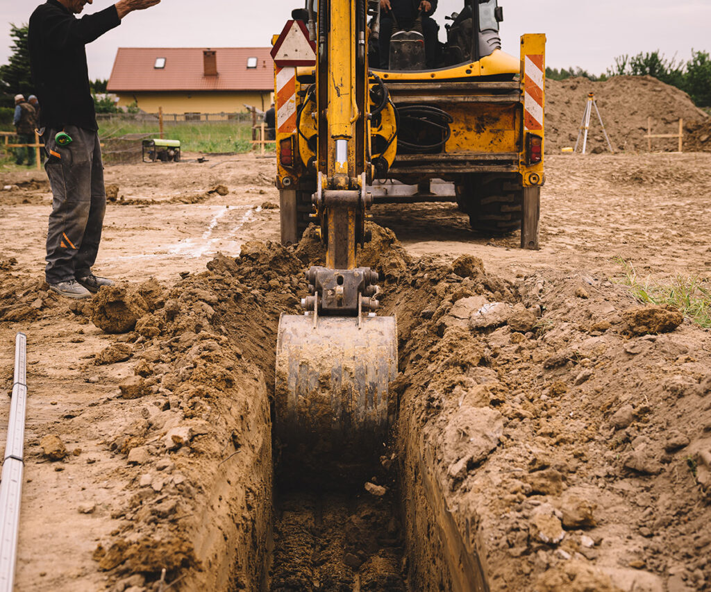 Construction worker overseeing excavation with heavy machinery on job site, emphasizing workplace safety and hazard identification in compliance with OSHA standards.
