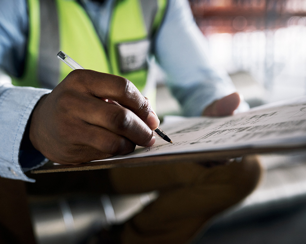Person in safety vest writing notes on clipboard, emphasizing workplace safety and compliance for OSHA regulations.