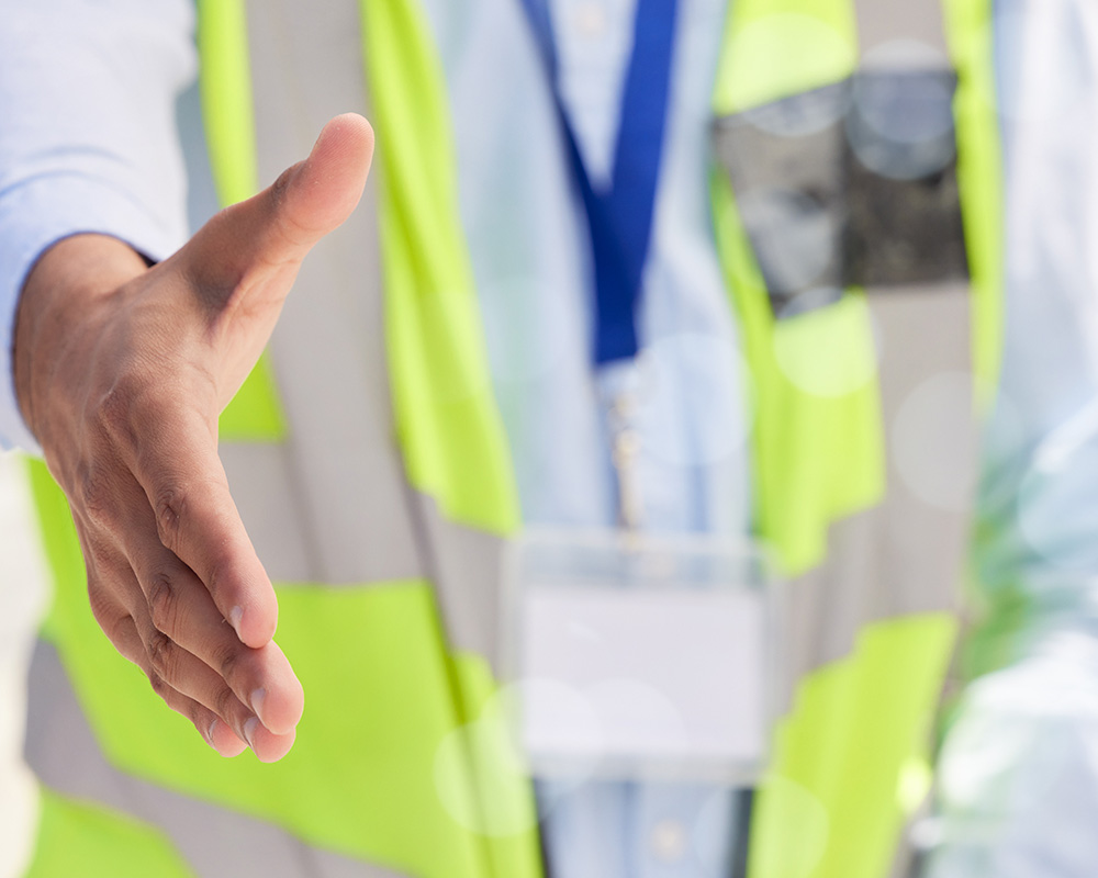 Hand reaching out for a handshake, with a focus on workplace safety attire, symbolizing collaboration and safety consulting services.