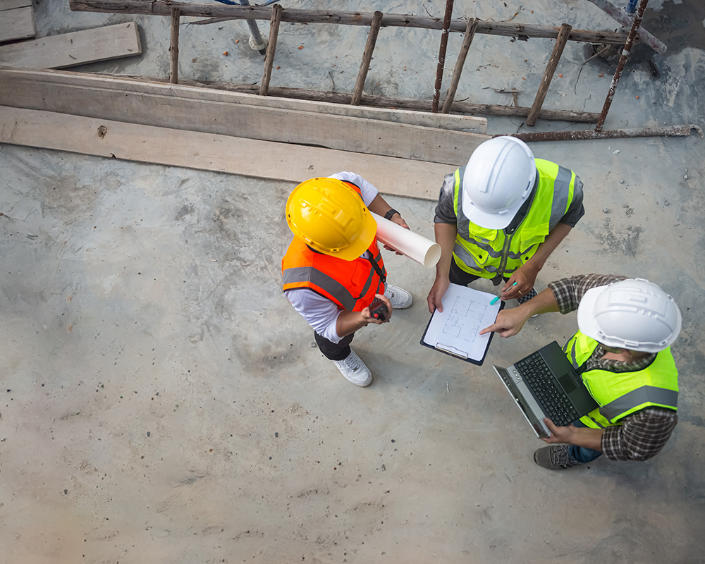 Construction workers in safety gear discussing project plans and OSHA compliance on a job site.