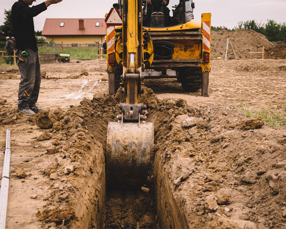 Construction worker operating excavator in trench on job site, emphasizing safety and compliance in workplace operations.