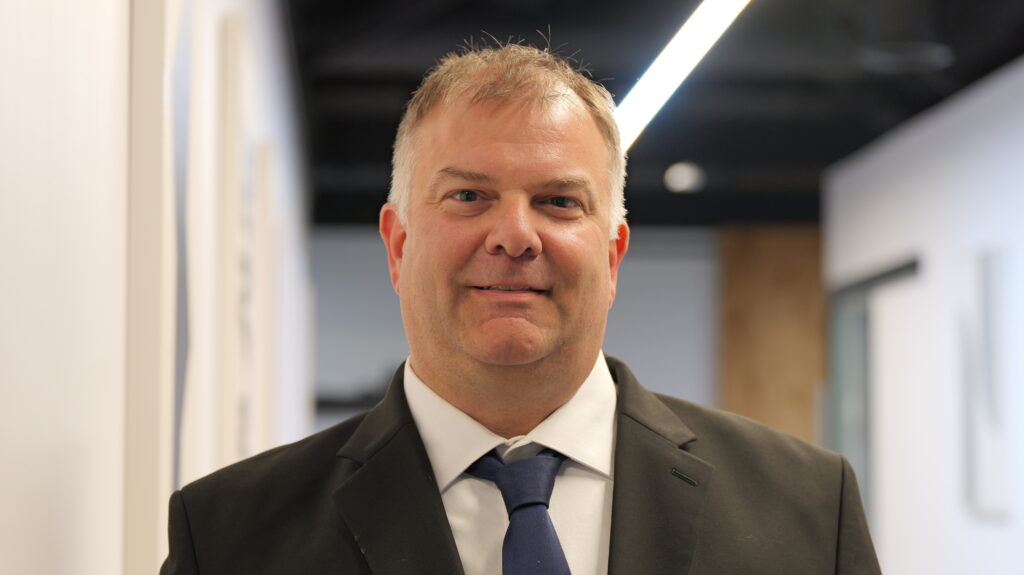 Professional man in a suit, smiling, in a modern office setting, representing Weinstein Safety Consulting's expertise in safety consulting and OSHA compliance.