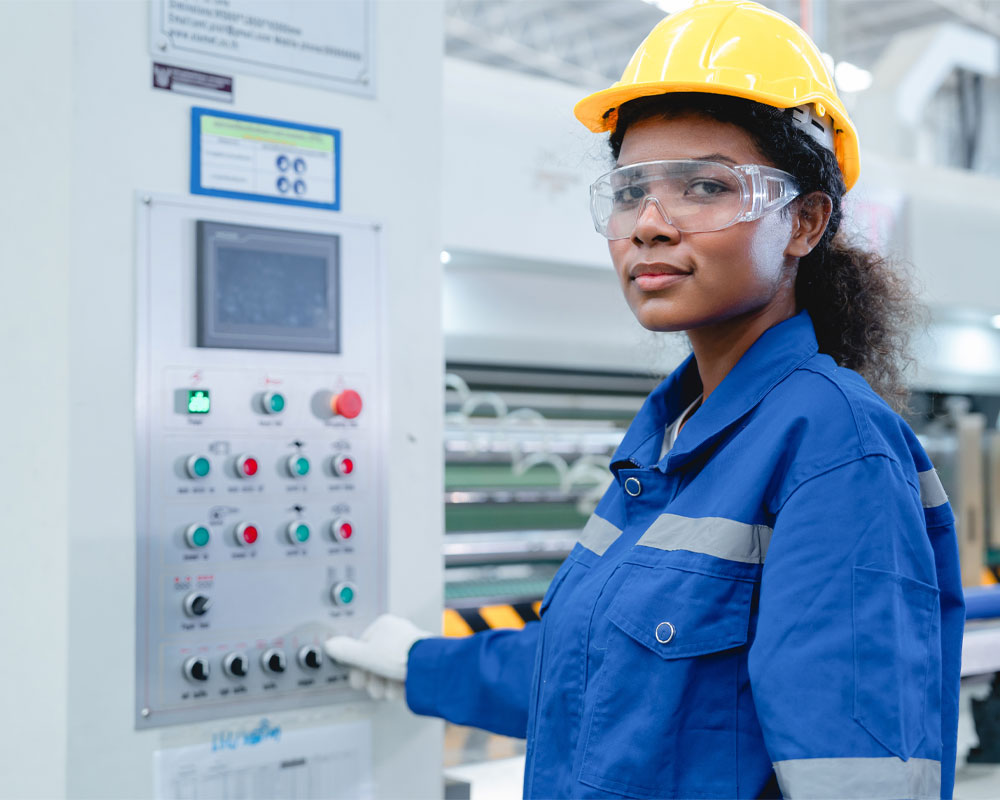 Woman in safety gear operating machinery control panel in industrial setting, emphasizing electrical safety and compliance with OSHA standards.
