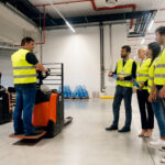 Forklift training session in progress, with employees wearing high-visibility safety vests and observing equipment operation