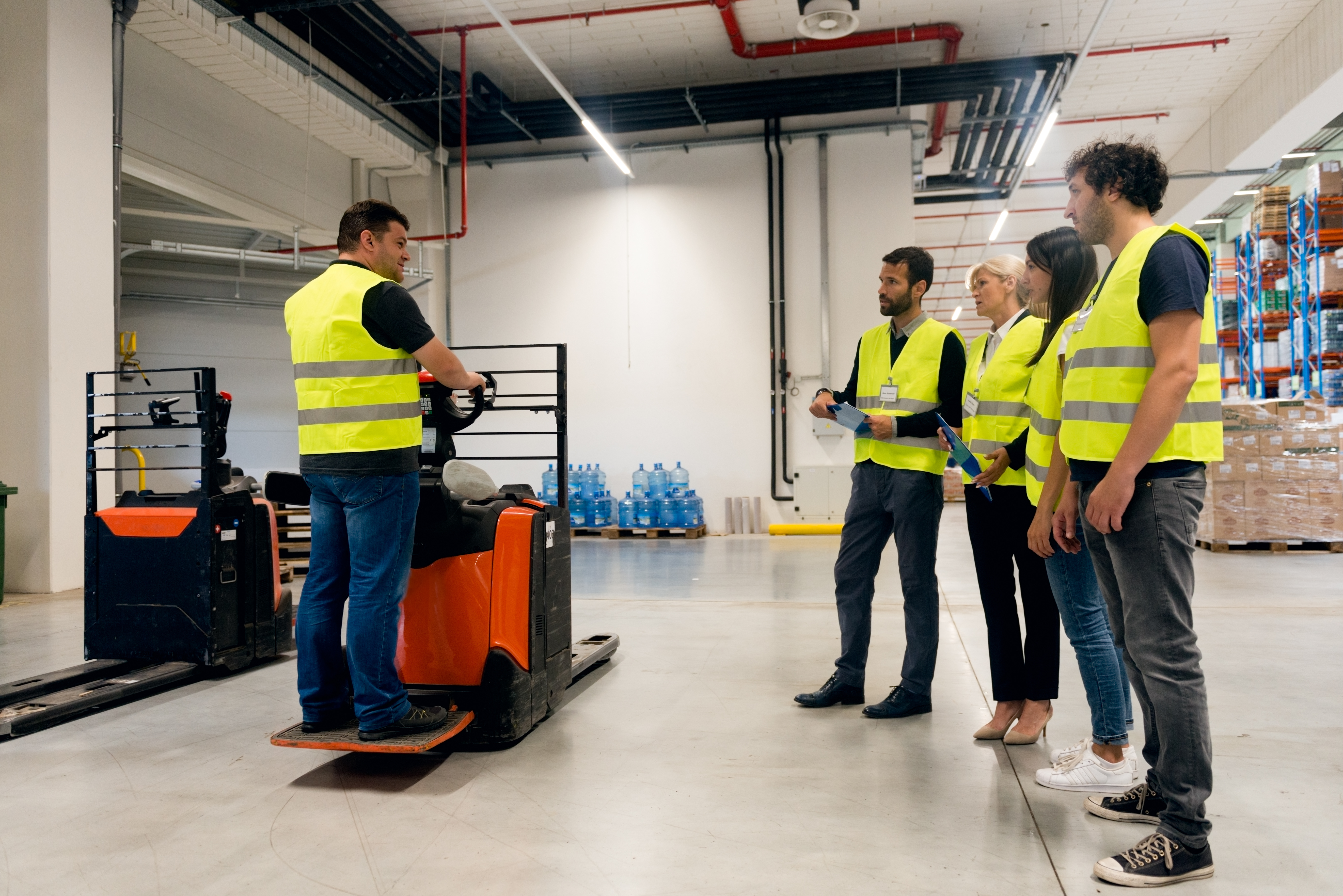 Forklift training session in a warehouse, with an instructor demonstrating operation to a group